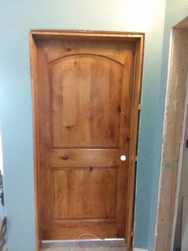 Wooden interior door with arched panels and a white knob in a light blue wall.