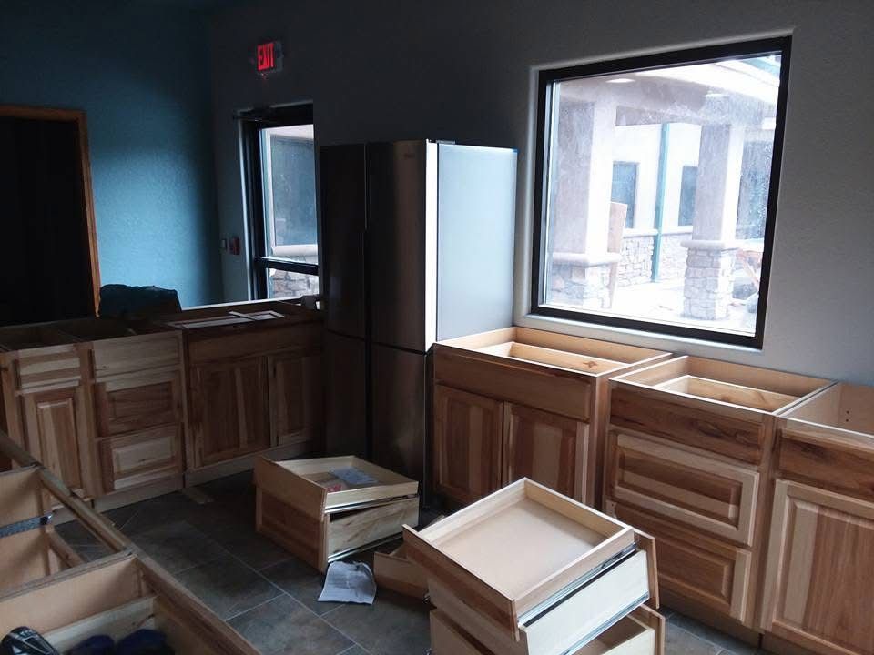 Damaged kitchen with broken cabinets and debris scattered on the floor by a large window
