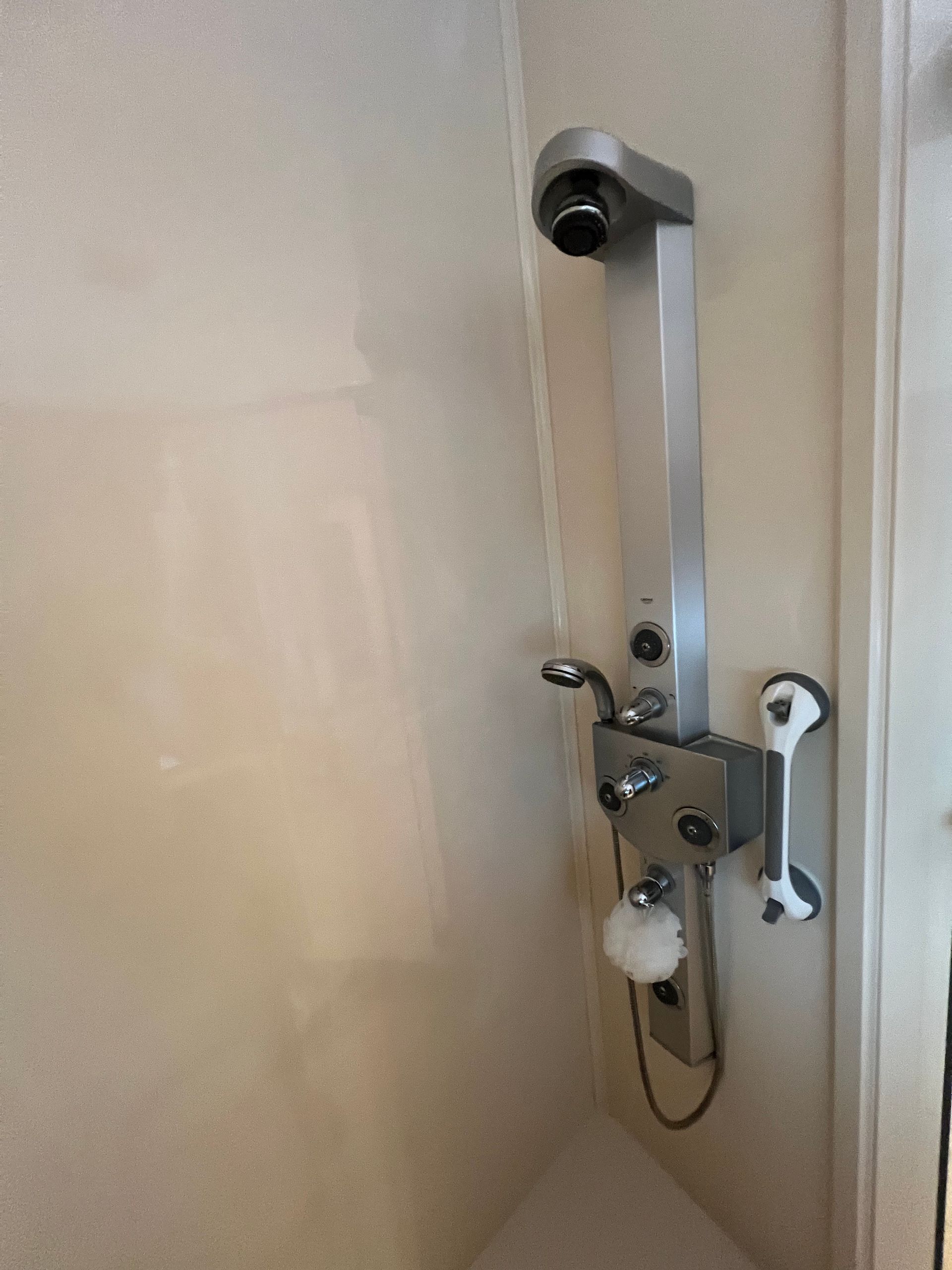 Wall-mounted shower seat in a beige shower stall with chrome hardware and white corner supports