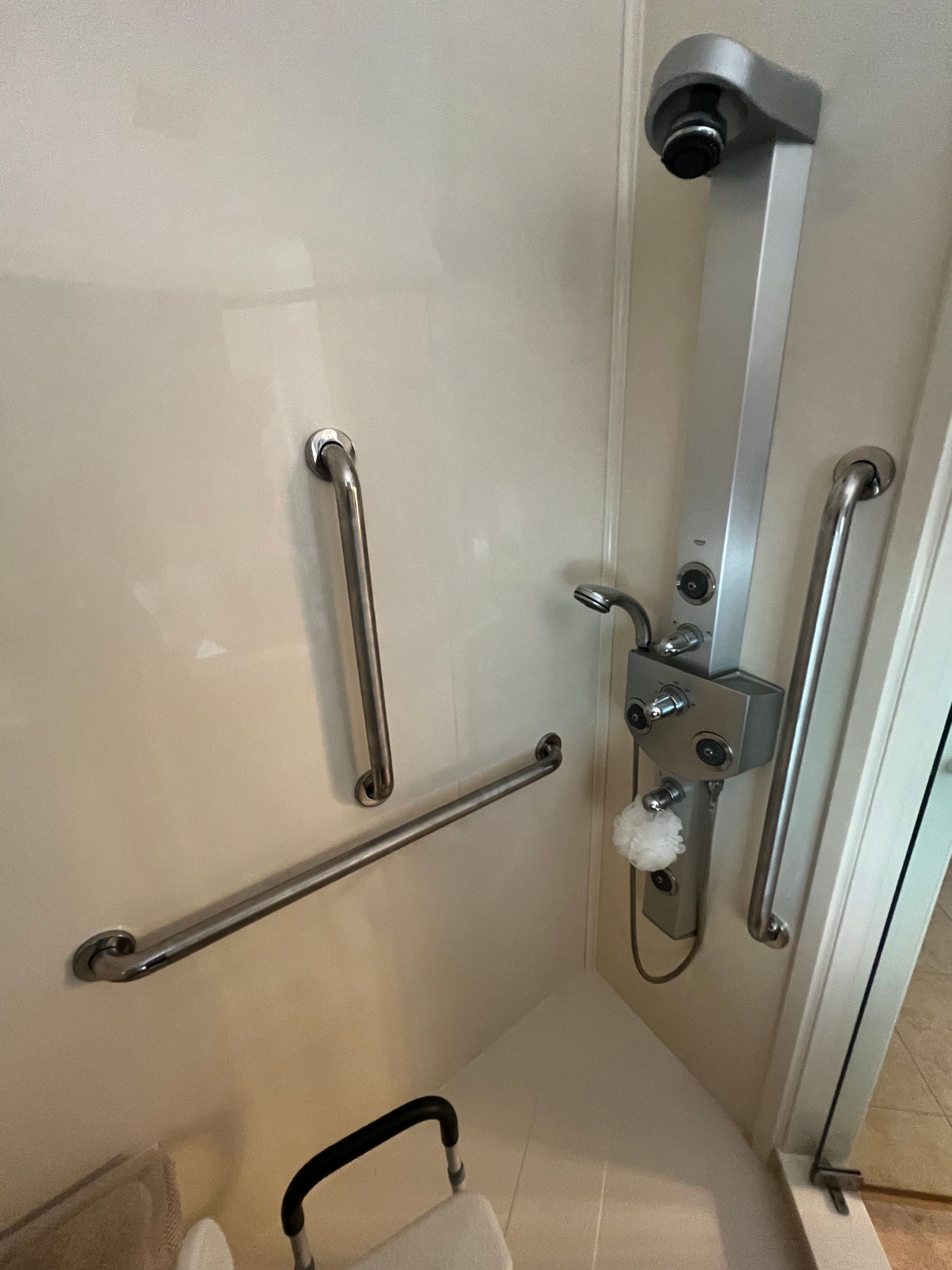 Accessible shower with grab bars, fold-down seat, and handheld showerhead in a tiled bathroom.