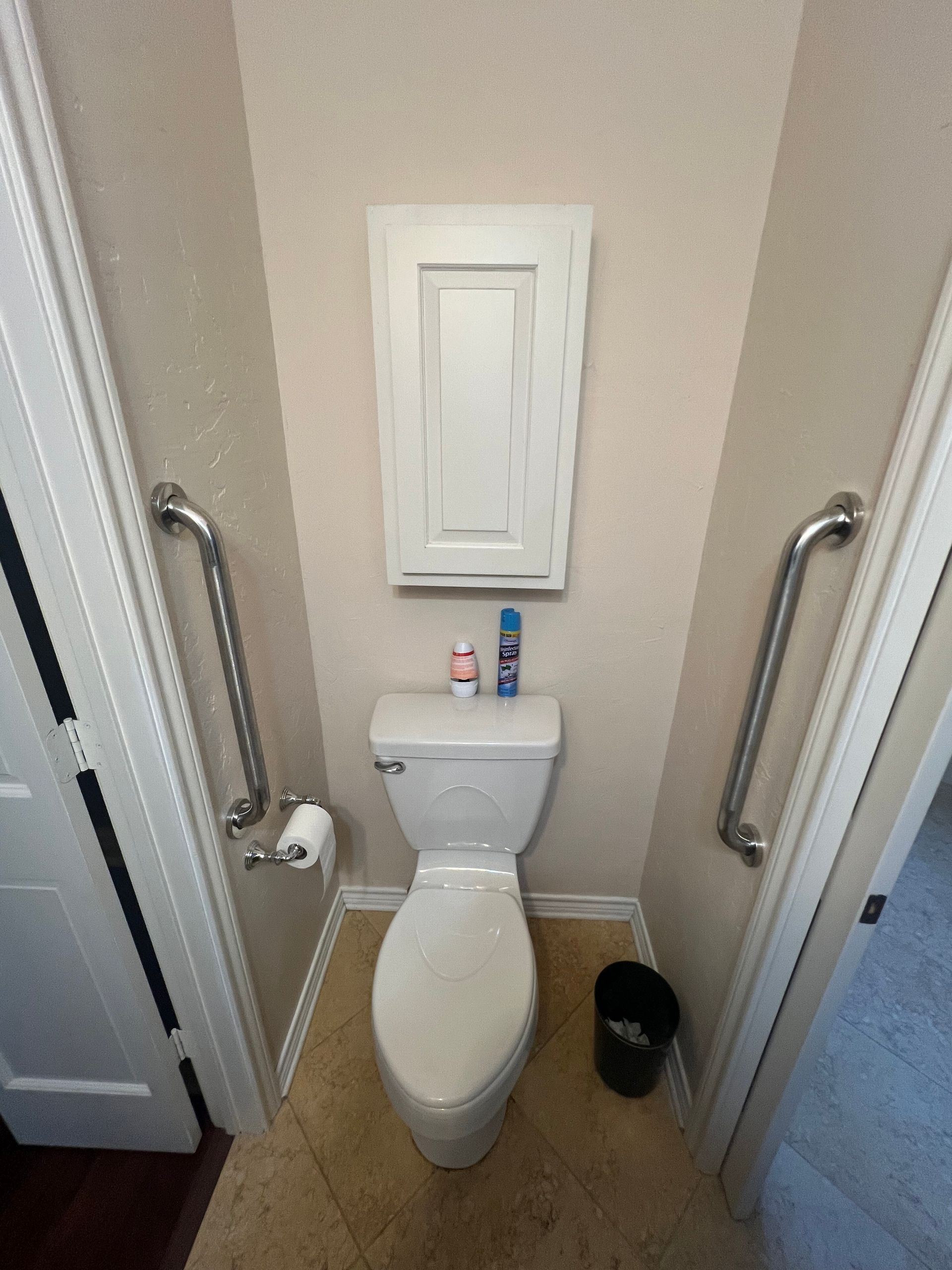 Small restroom with a white toilet, wall cabinet above, and grab bars on both sides.