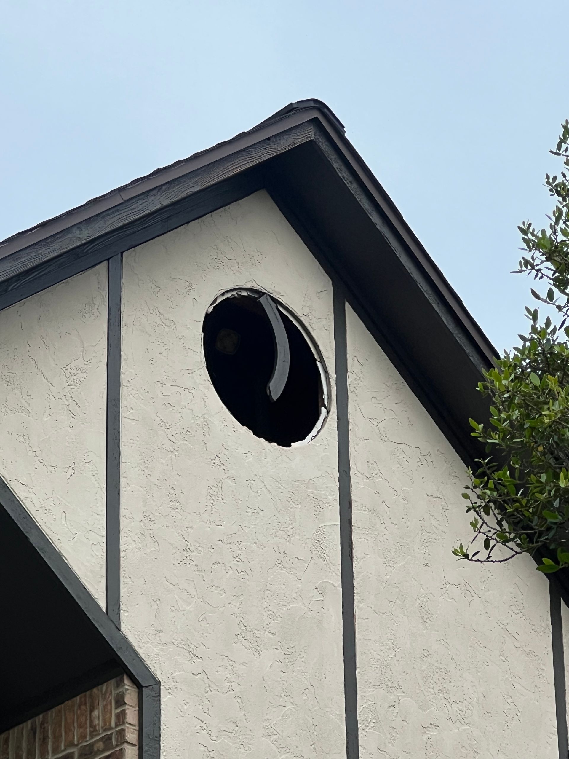 White house gable with a round attic vent against a blue sky