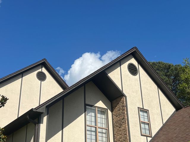 Cream house with steep dark roofs against a blue sky and a white cloud