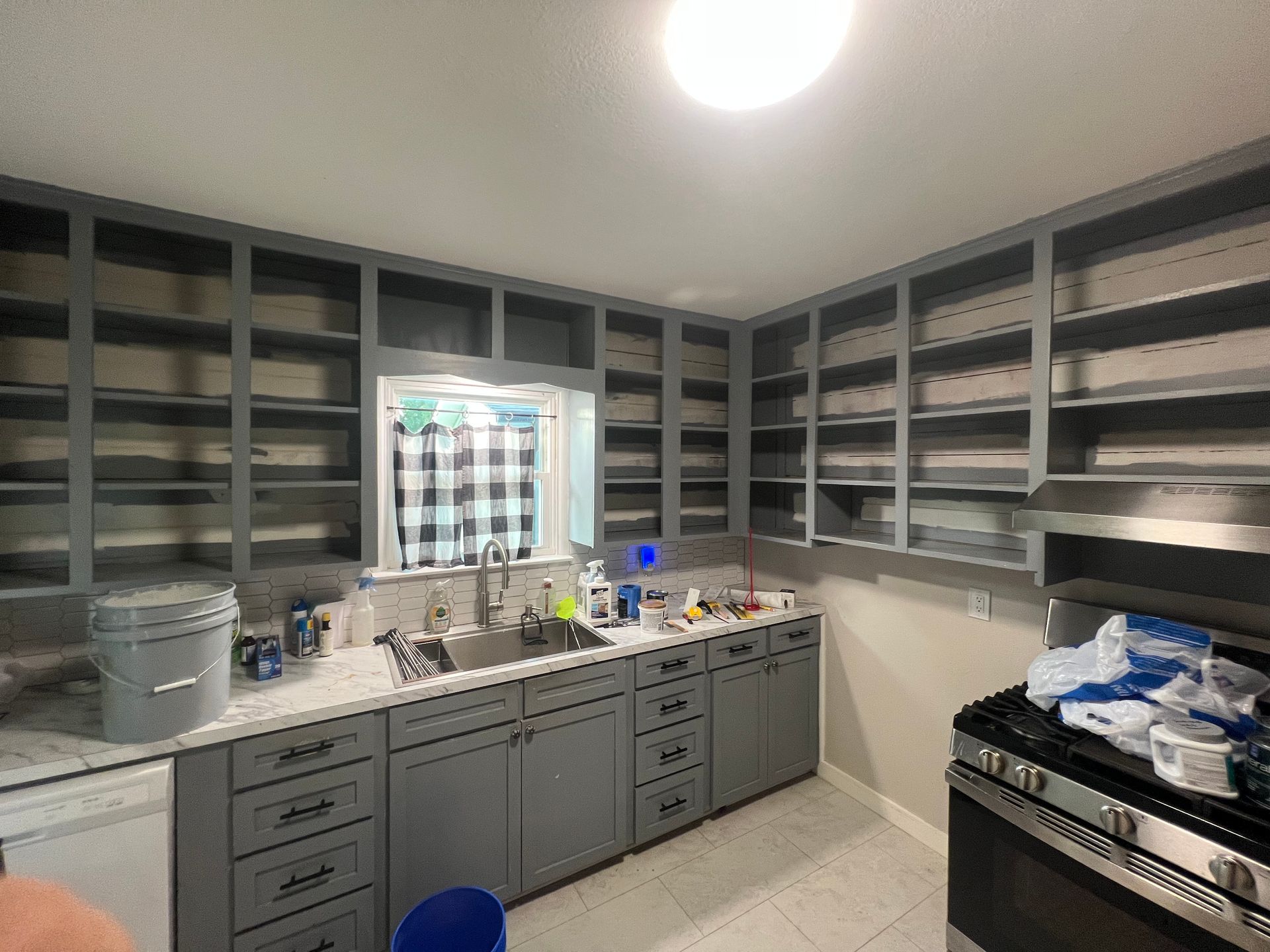 Empty kitchen with gray cabinets, white countertops, sink, and a stove with a bag of blue items on top.
