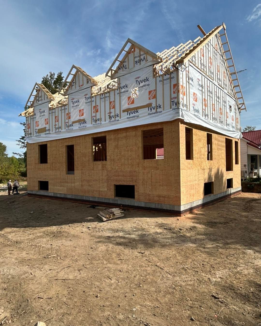 Construction d'un bâtiment à deux étages avec charpente en bois apparente, bardage et toiture partiellement construite, sur fond de ciel bleu.