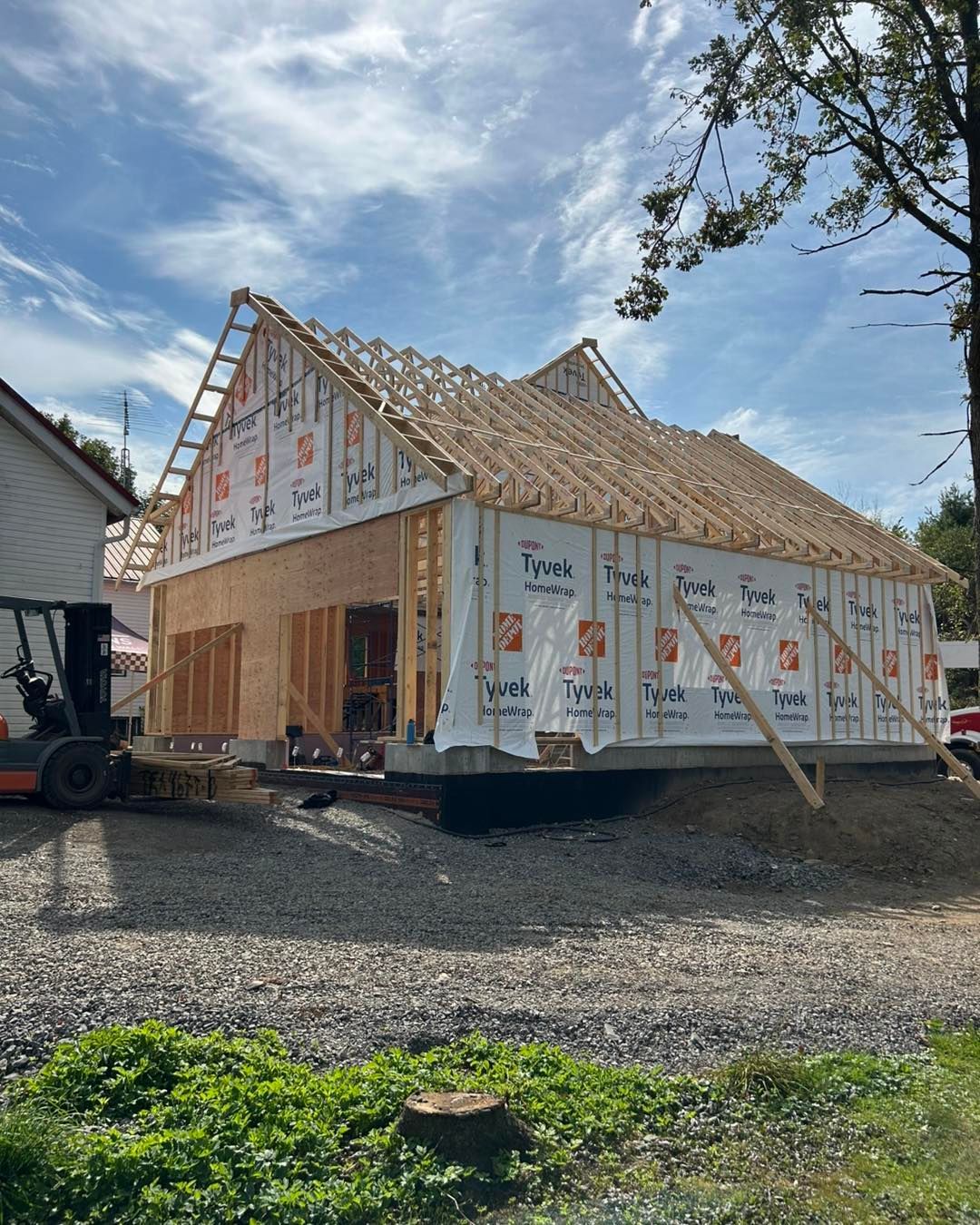 Bâtiment en construction : ossature bois recouverte d’un film Tyvek et charpente apparente, ciel bleu en arrière-plan.