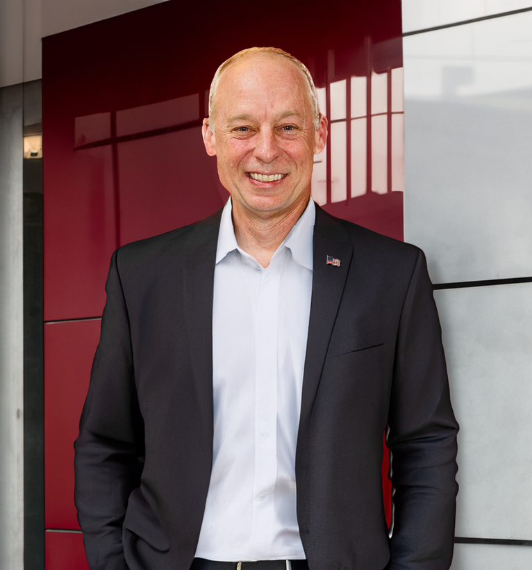 A man in a suit is standing in front of a red wall