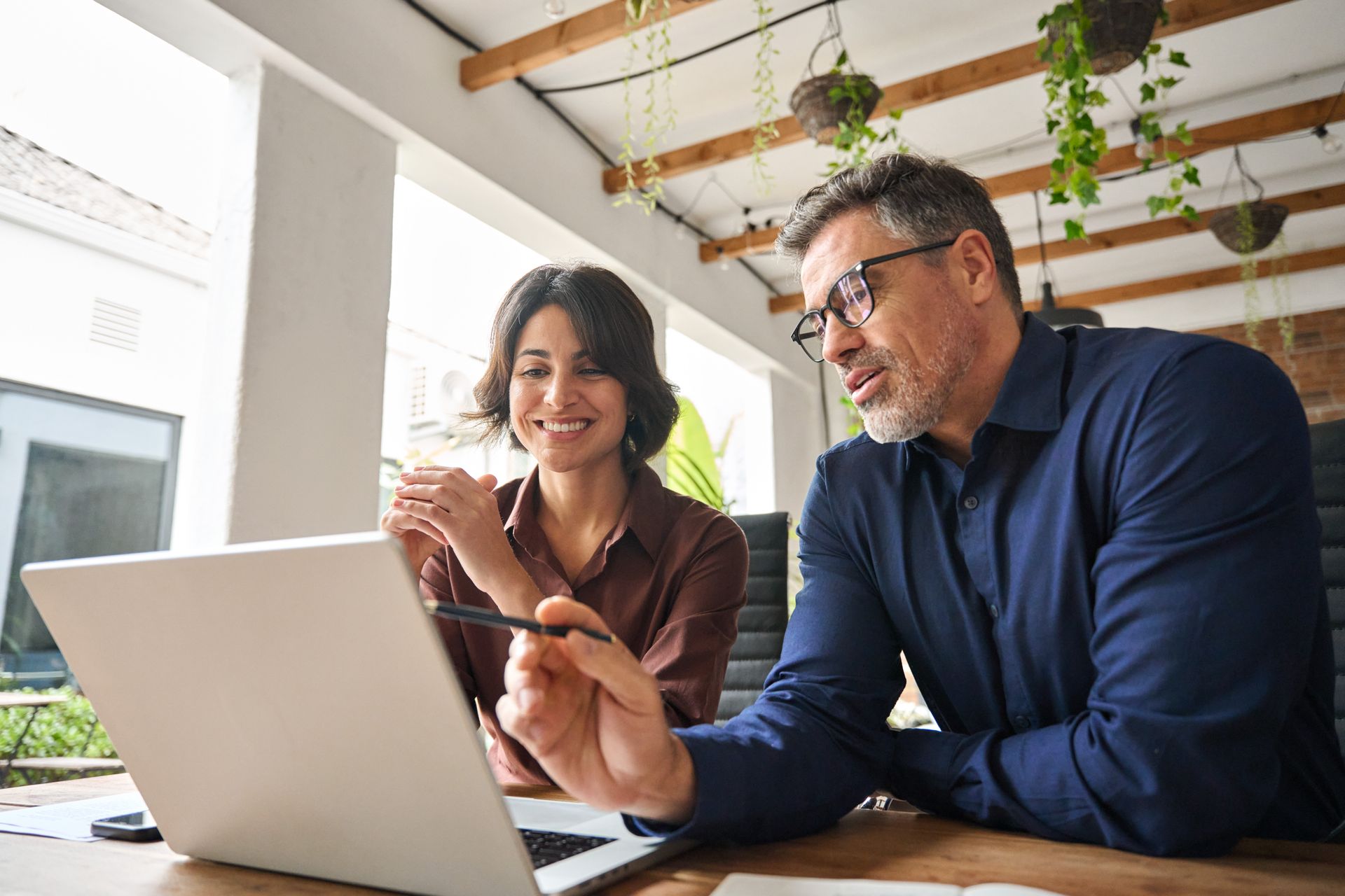 A man and a woman are sitting at a table looking at a laptop computer.