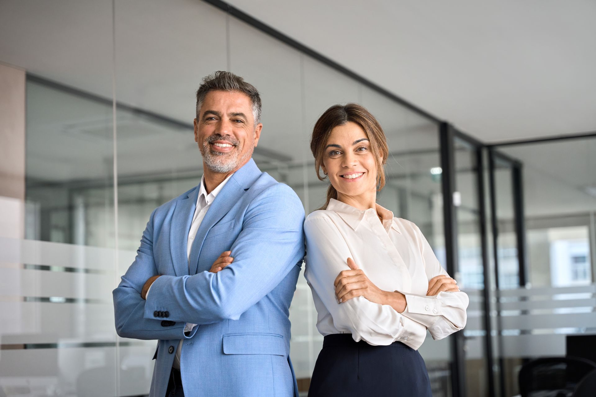 A man and a woman are standing next to each other in an office with their arms crossed.