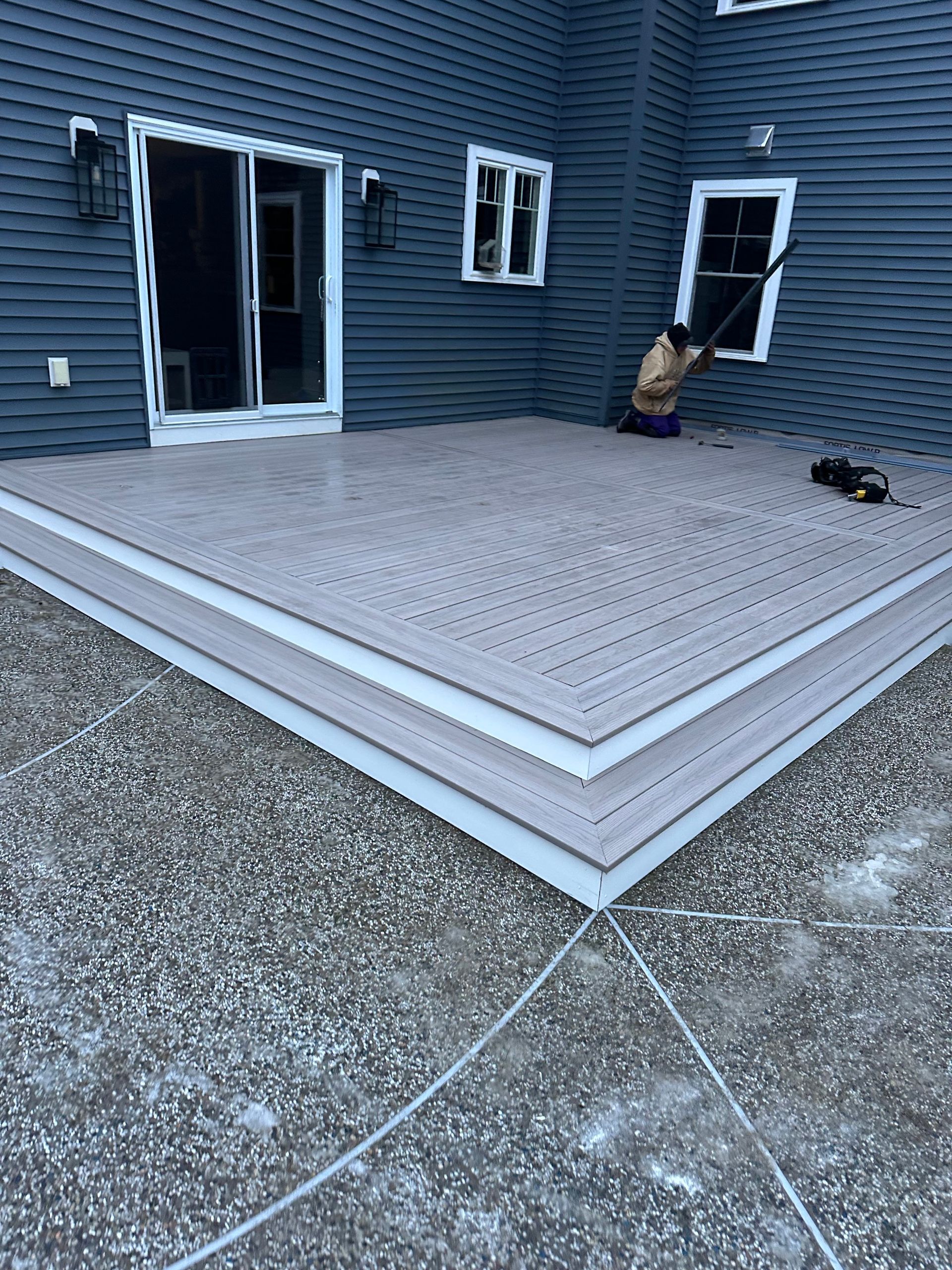 Gray composite deck with a person cleaning windows on a blue siding house.