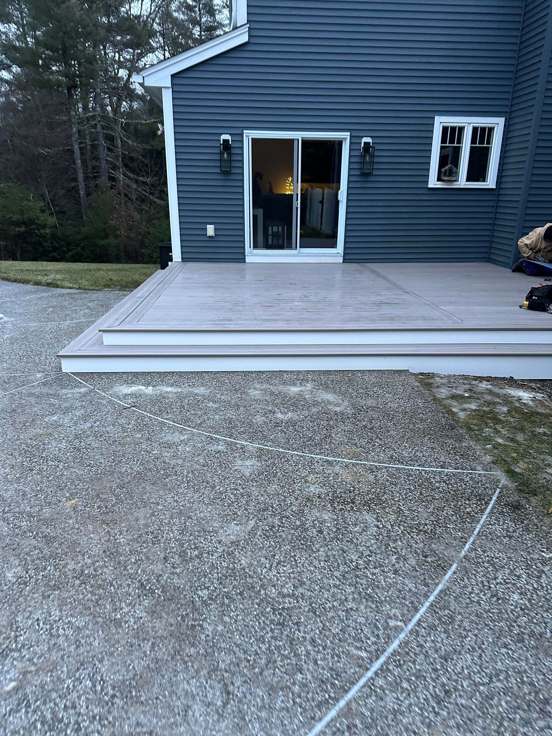 A gray composite deck with two steps leads to a house with blue siding and a sliding glass door.