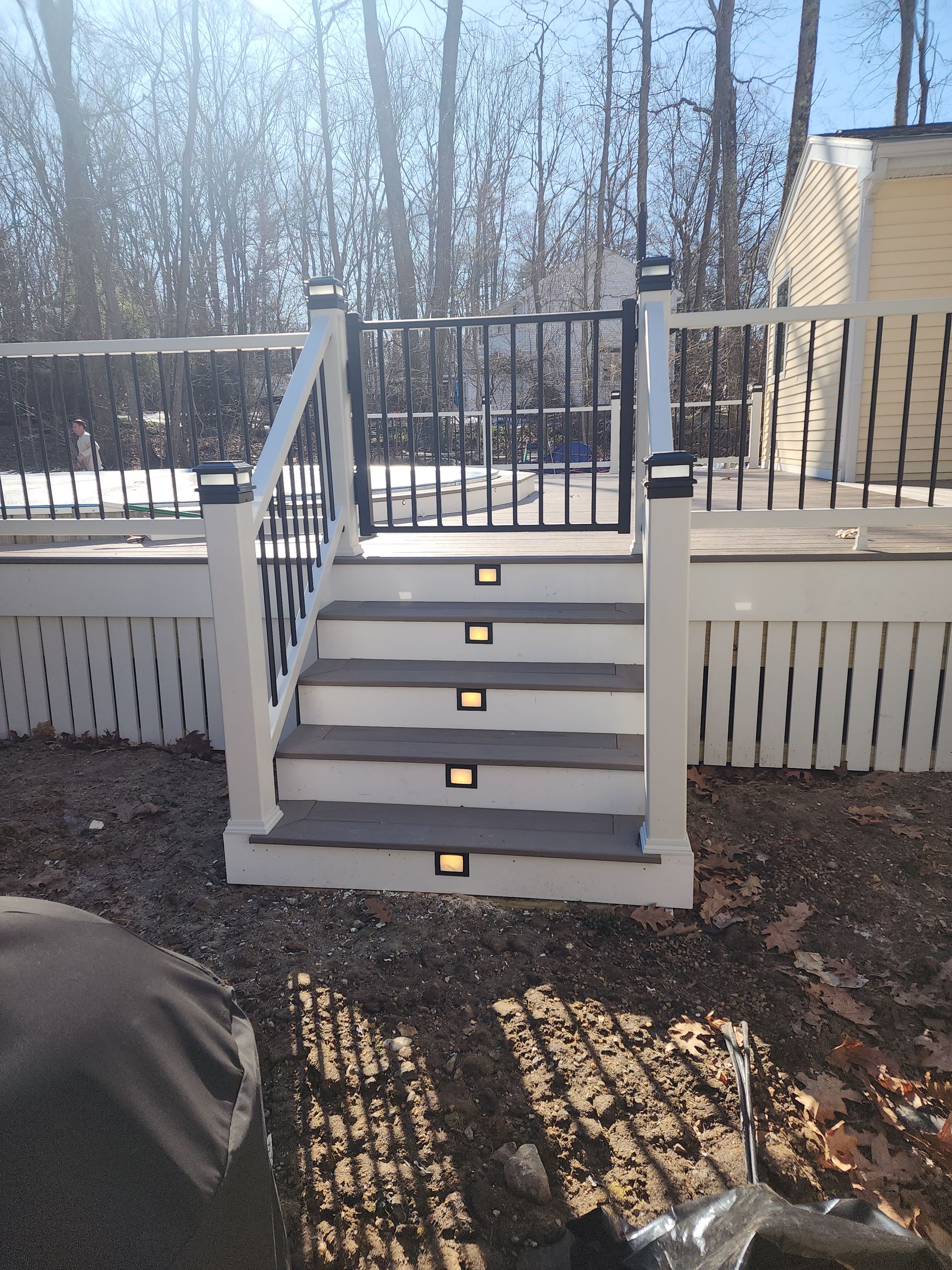 Composite deck stairs with built-in lights leading to a gate, bordered by white railings and black accents.
