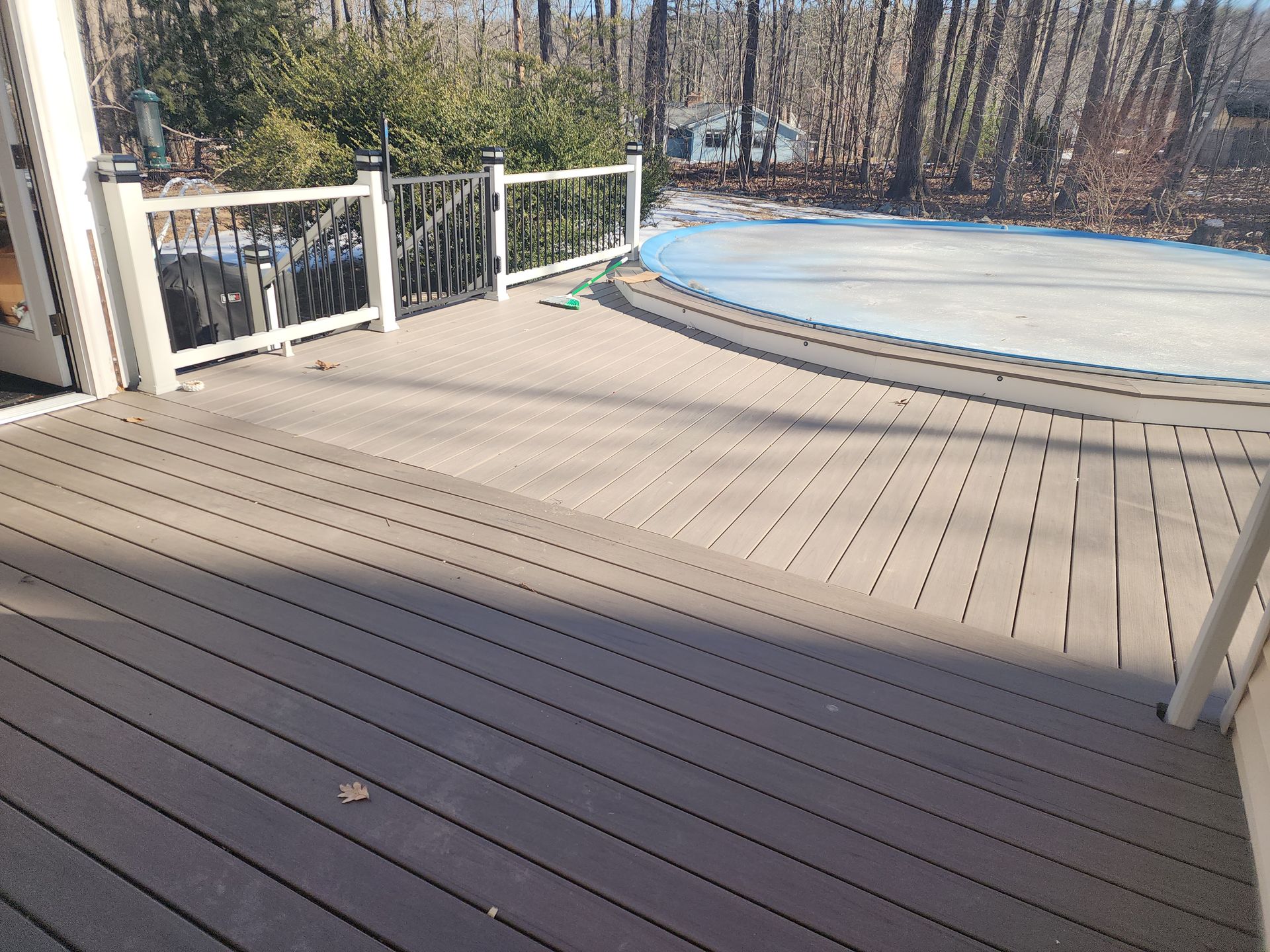 A composite deck with a white railing overlooks a pool with a blue cover, set amongst trees.