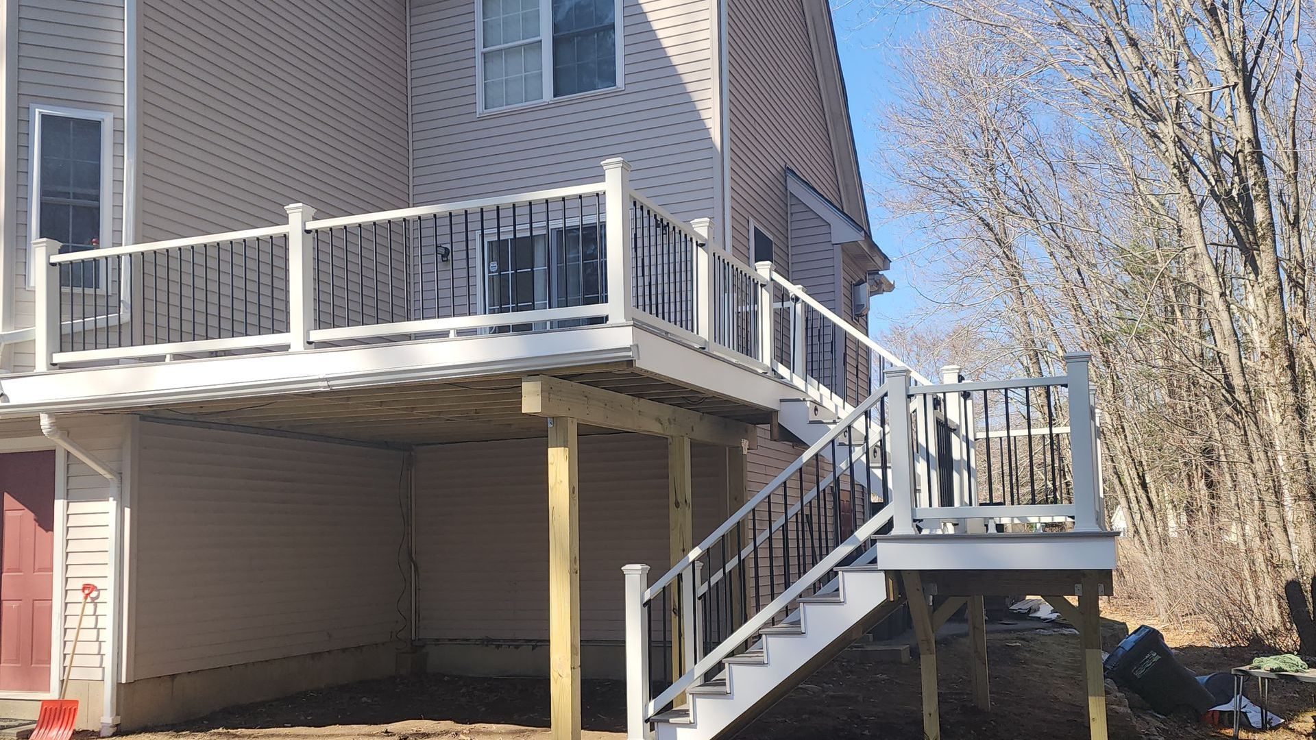Two-story house with a wooden deck and stairs. White and black railing. Daytime, outdoor setting.