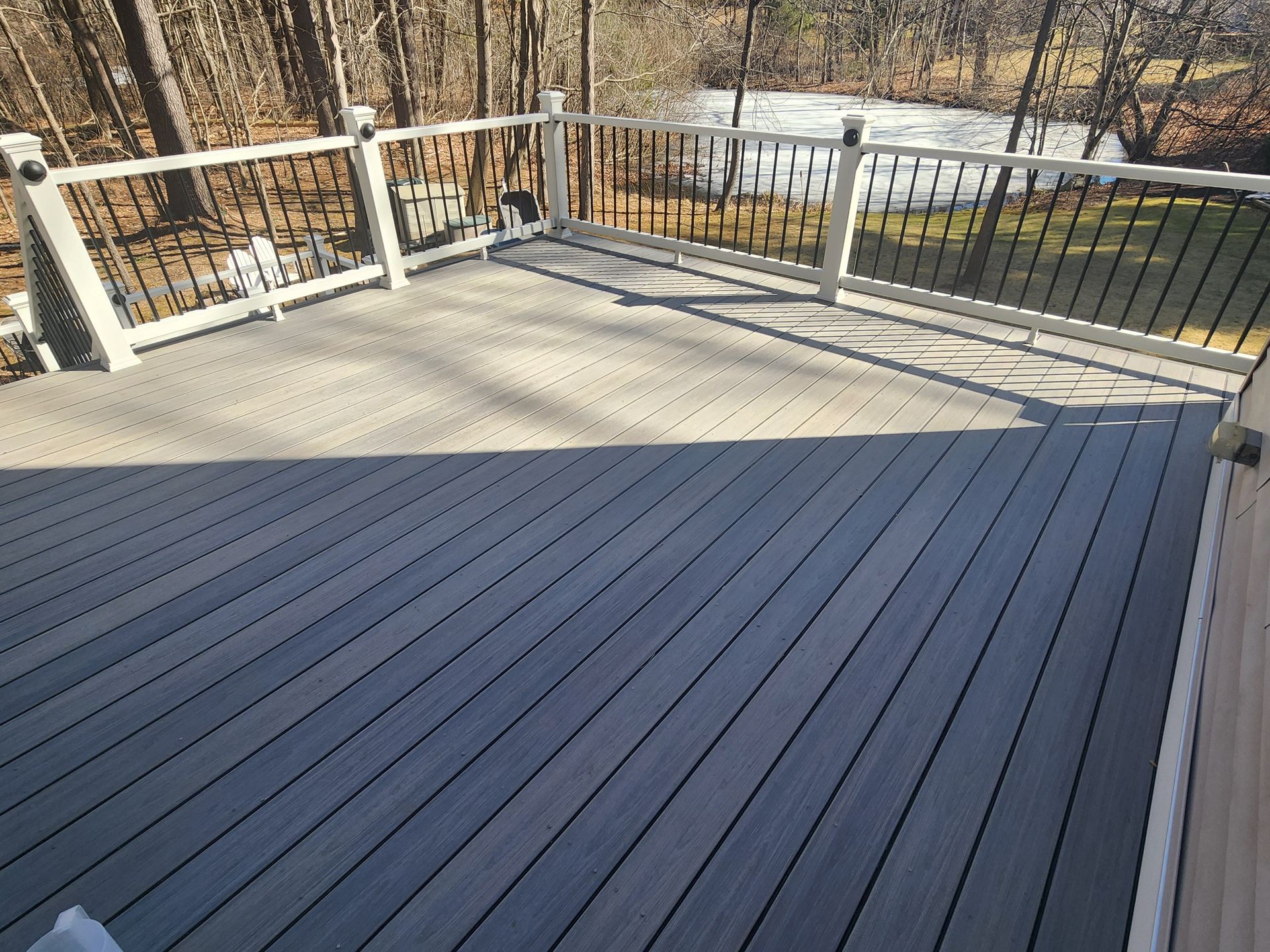 Gray composite deck with white railing, black balusters, and a forest background.