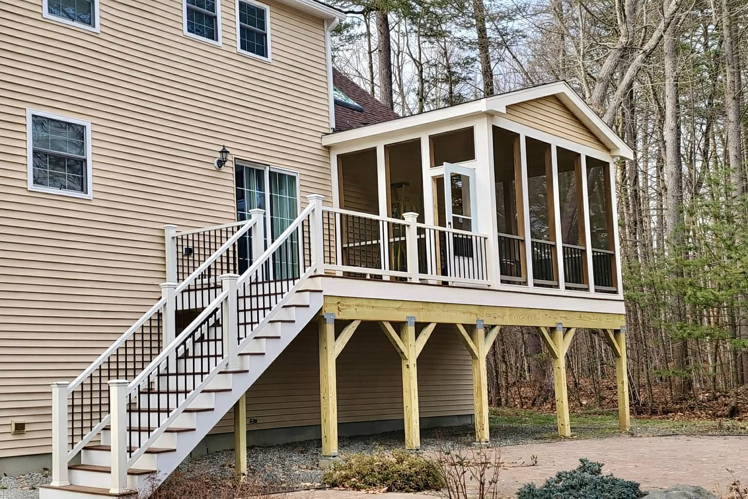 Back deck with white stairs and screened porch attached to a tan house in a wooded yard