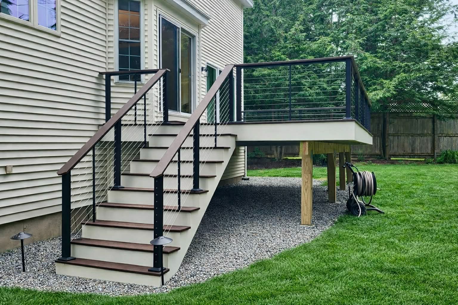 Backyard deck stairs with black railing leading from a beige house onto a gravel and grass yard
