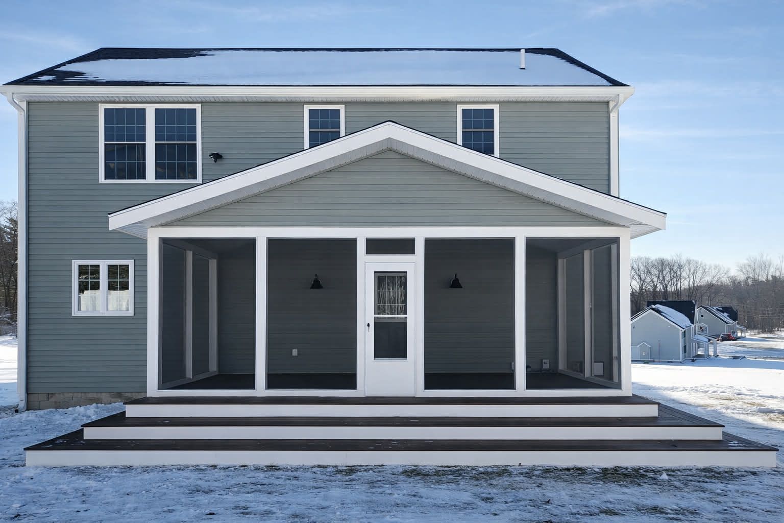 Snowy two-story gray house with a white front porch and black roof, viewed from the front.