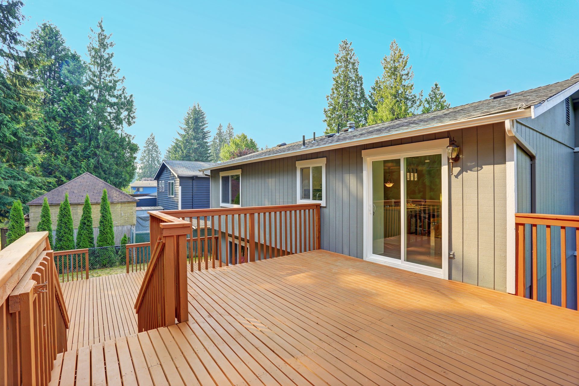 Spacious wooden backyard deck attached to house with sliding glass door and railing. Spacious wooden backyard deck attached to house with sliding glass door and railing.