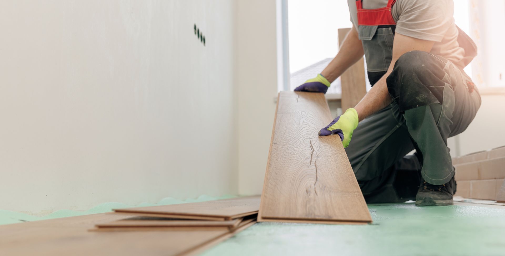 Worker installing wood plank flooring inside a residential room.
