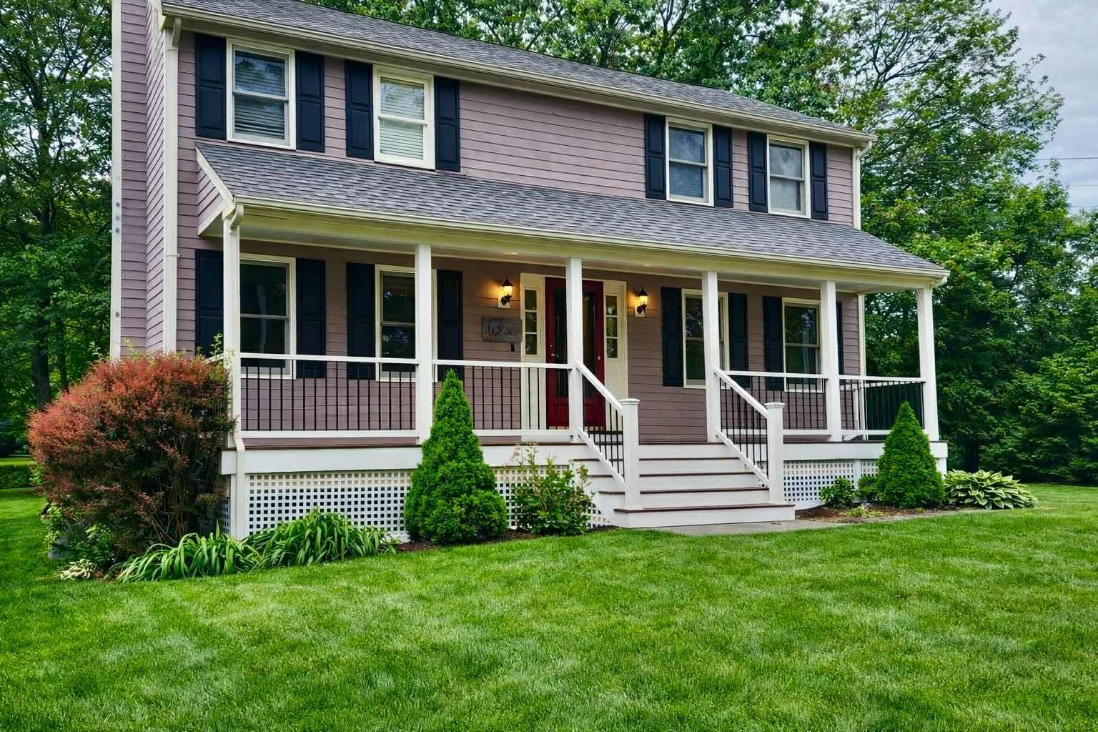 Two-story suburban house with white porch, red shutters, and a green lawn