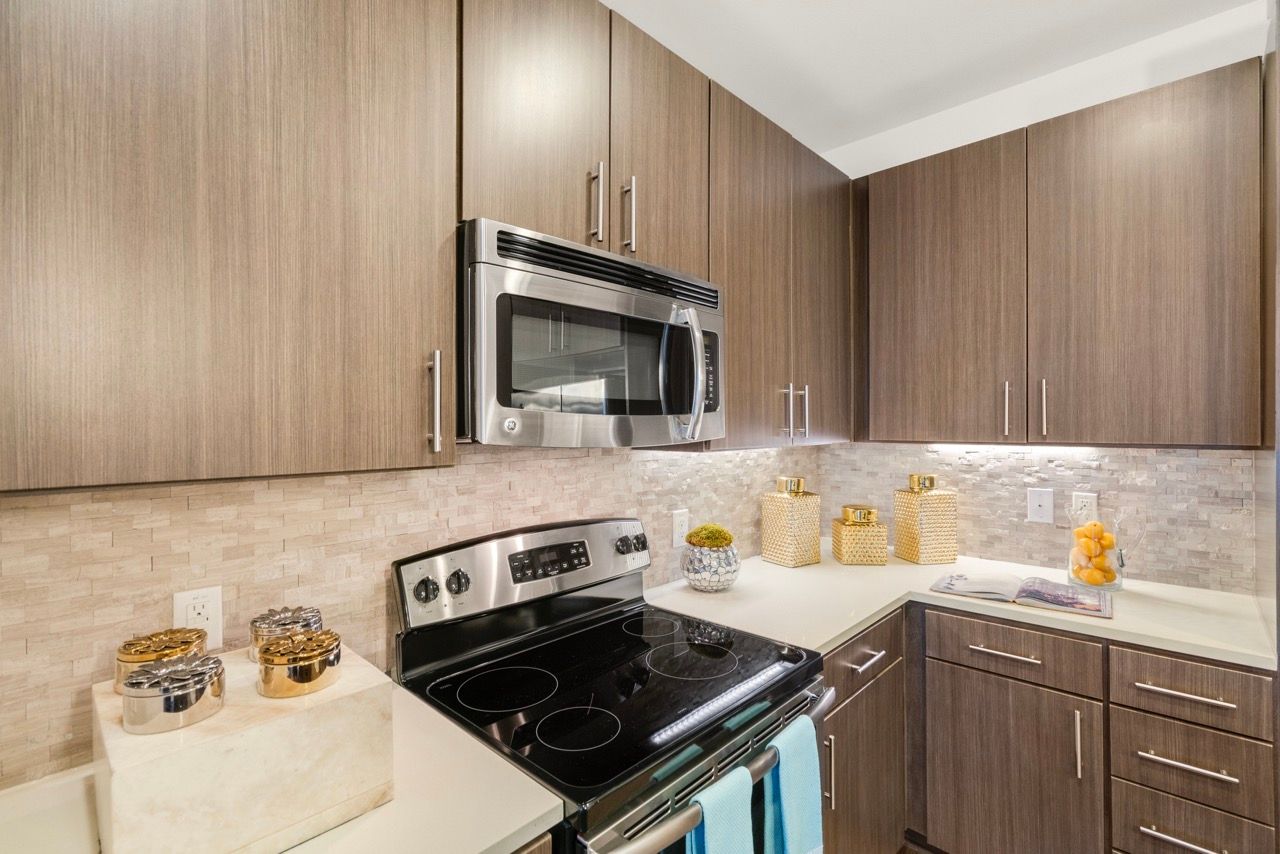 Modern apartment kitchen with dark wood cabinets, stainless steel microwave, and stove.