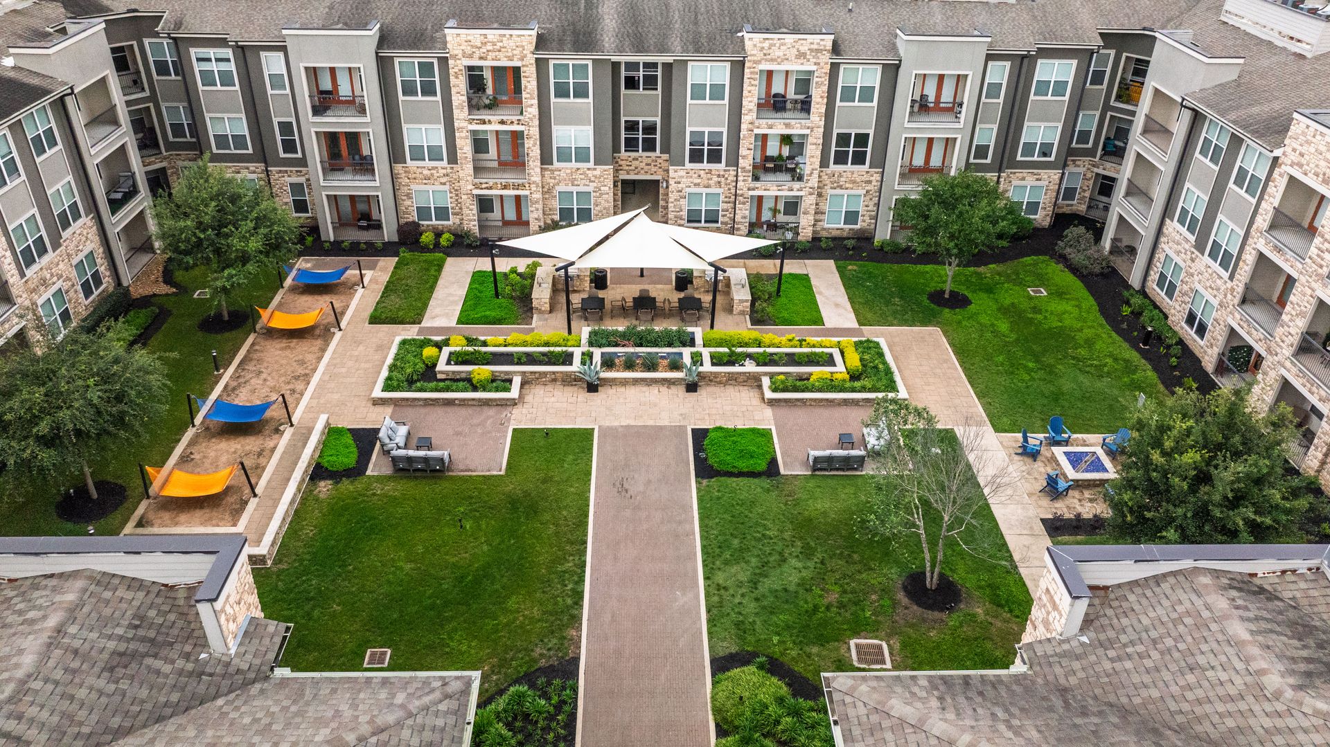 Courtyard with central walkway, green lawns, benches, and gazebo surrounded by apartment buildings at Olympus Grand Crossing, offering apartments near Houston, TX.