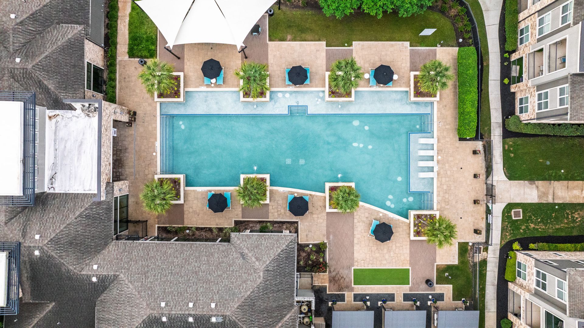 Aerial view of a turquoise swimming pool in a courtyard surrounded by buildings and lounge chairs at Olympus Grand Crossing, offering Katy apartments for rent.