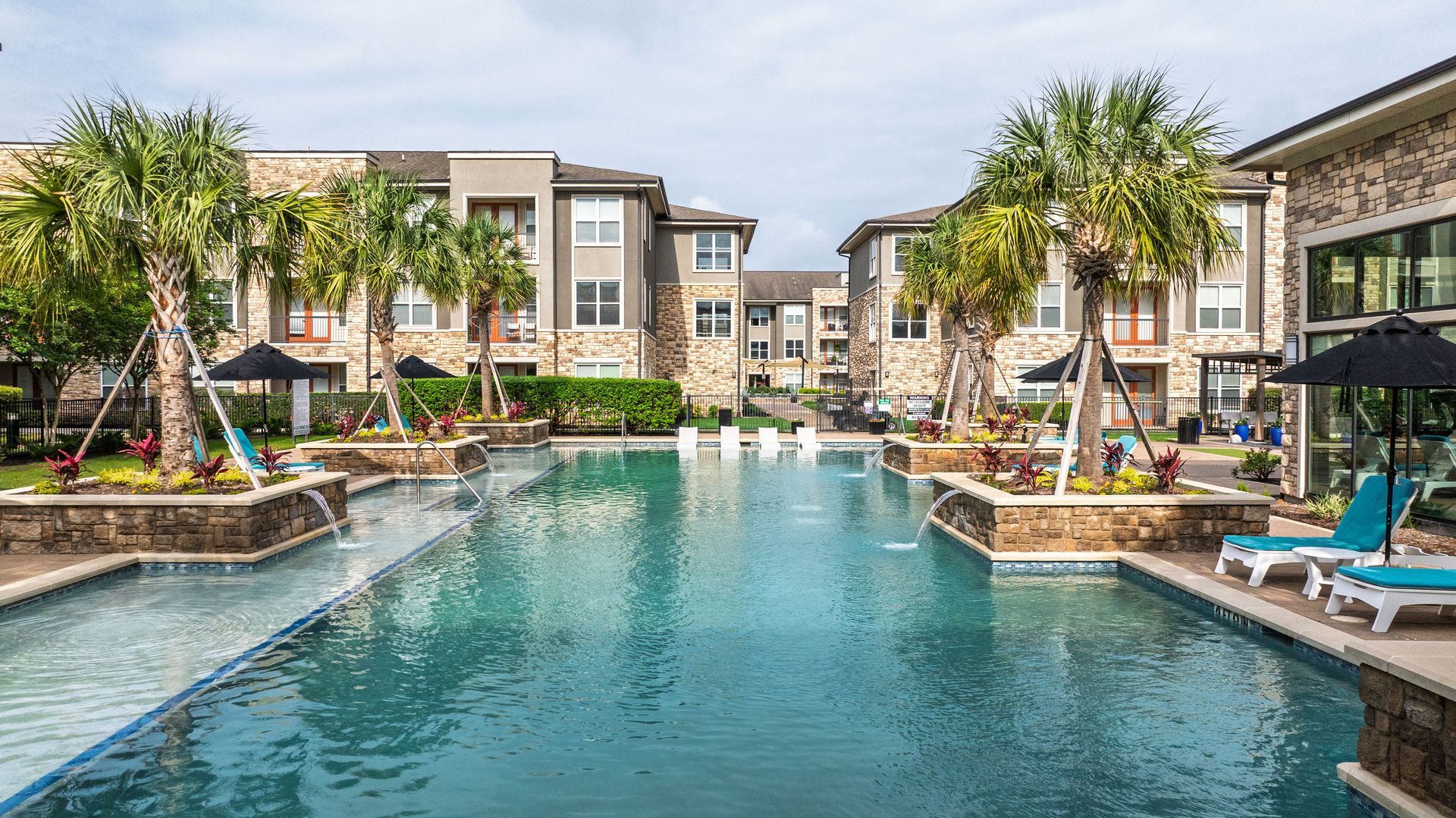 Luxury apartment pool with palm trees, lounge chairs, and turquoise water at Olympus Grand Crossing, offering Katy apartments for rent.