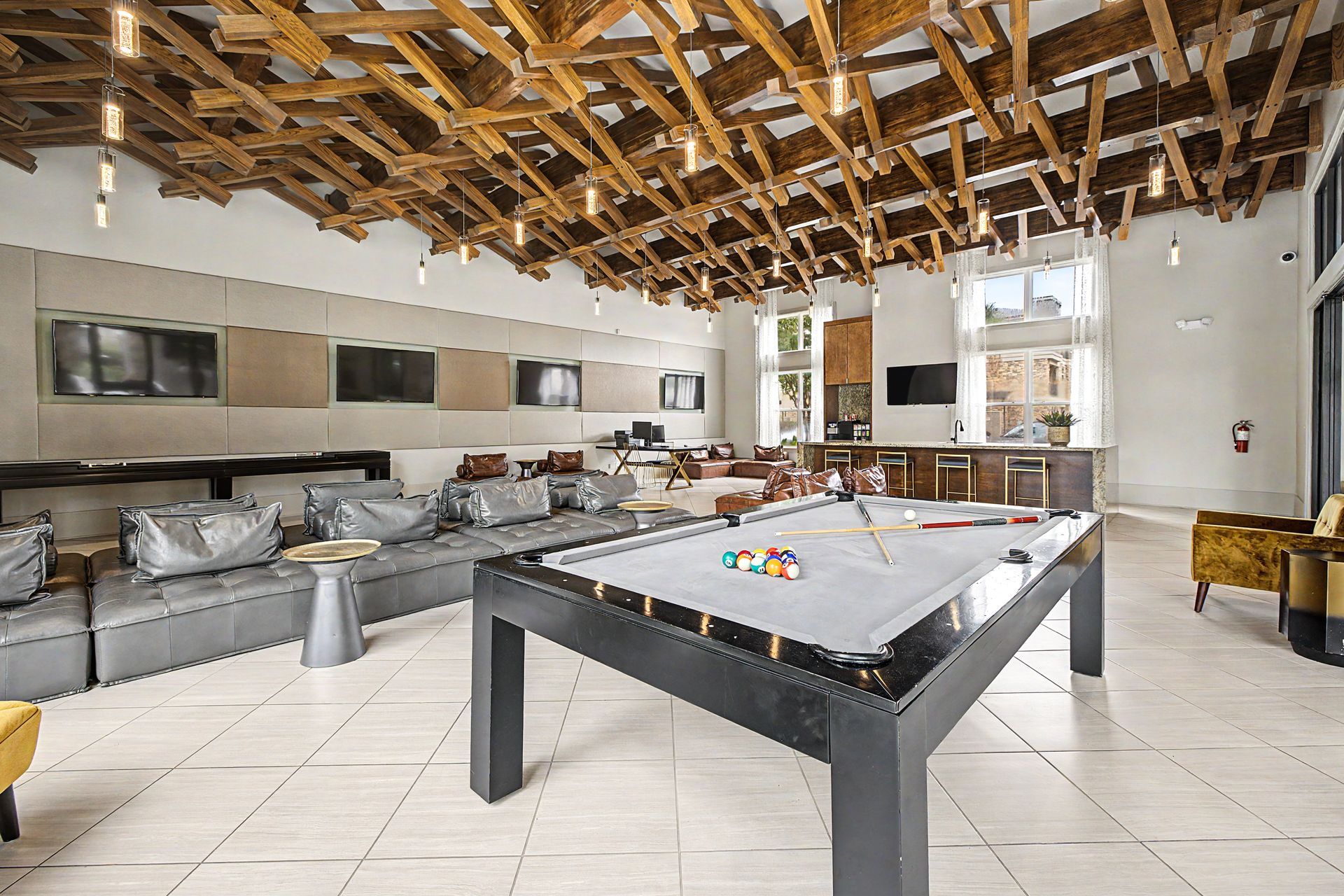 Modern loft game room with pool table, gray sectional sofa, and exposed wooden ceiling at Olympus Grand Crossing, offering pet-friendly apartments in Katy, TX.