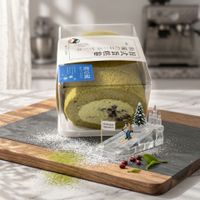 Matcha Swiss roll cake in clear packaging on a wooden board with powdered sugar and holiday decor