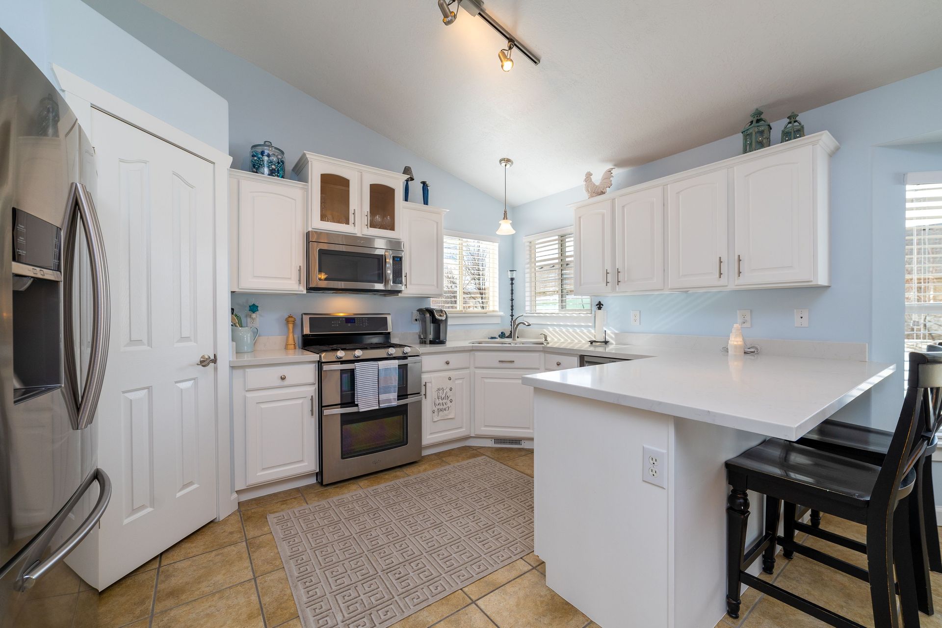 Bright white kitchen with stainless appliances, island counter, and woven rug in a sunlit home interiors rooms.