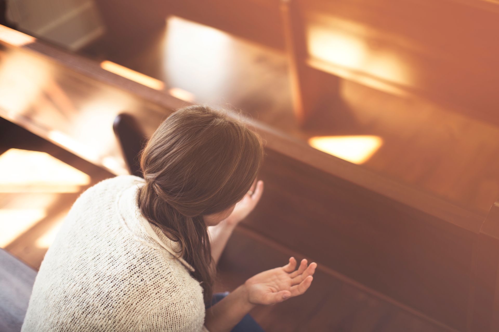Person in orange shirt resting face on a church pew beside a Bible.