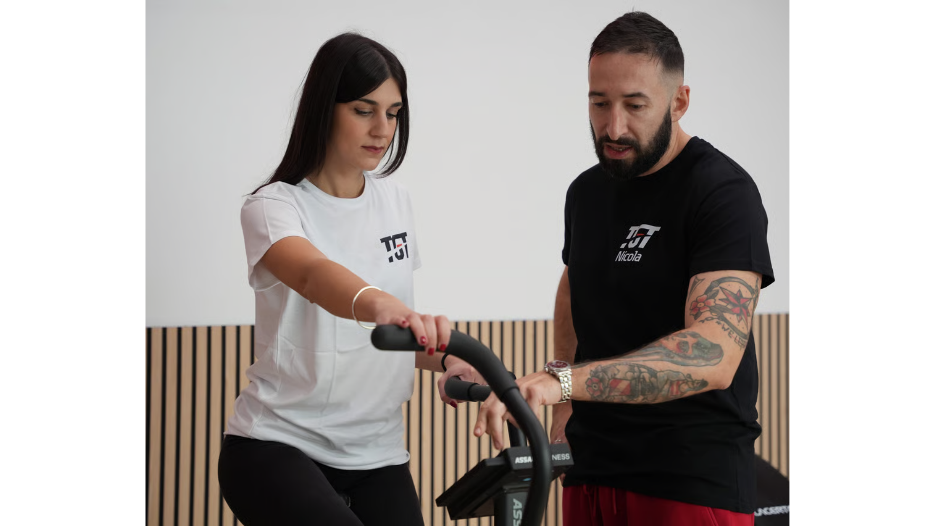 Un istruttore impartisce istruzioni a una persona che utilizza un attrezzo ginnico fisso in una palestra.