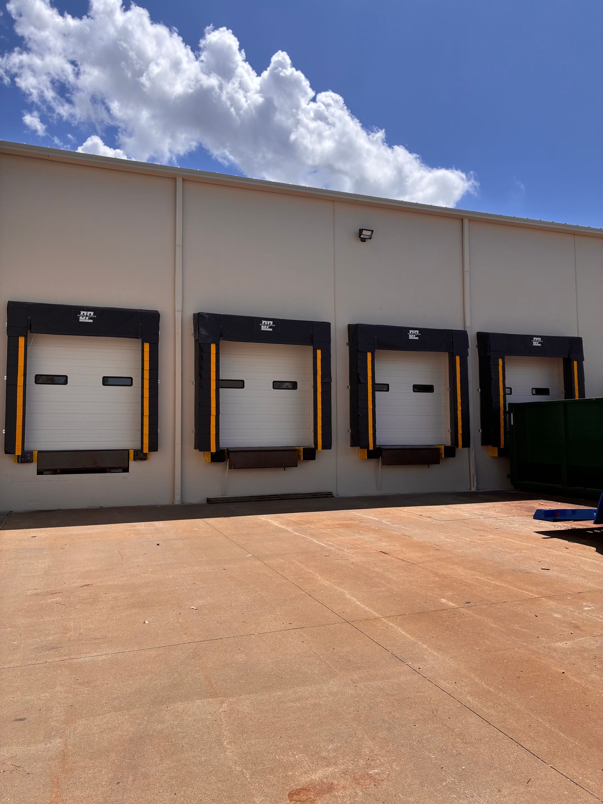 Four loading dock bays on a beige warehouse exterior under a blue sky, with a gravel lot in front.