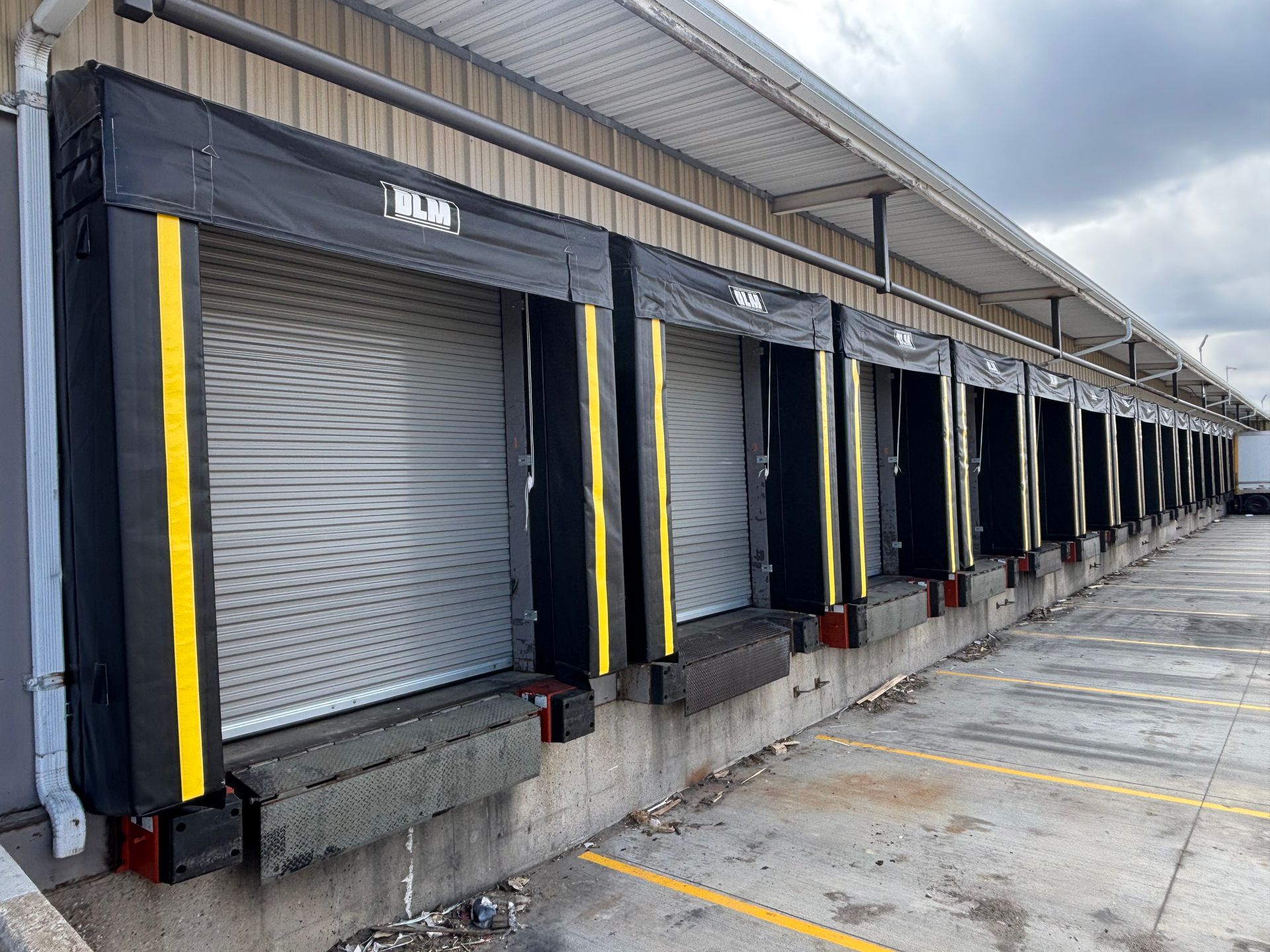 Loading dock with multiple closed roll-up doors and yellow safety stripes along a warehouse wall