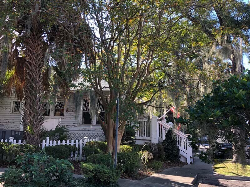 Tree-shaded house with white picket fence and porch in a leafy residential yard