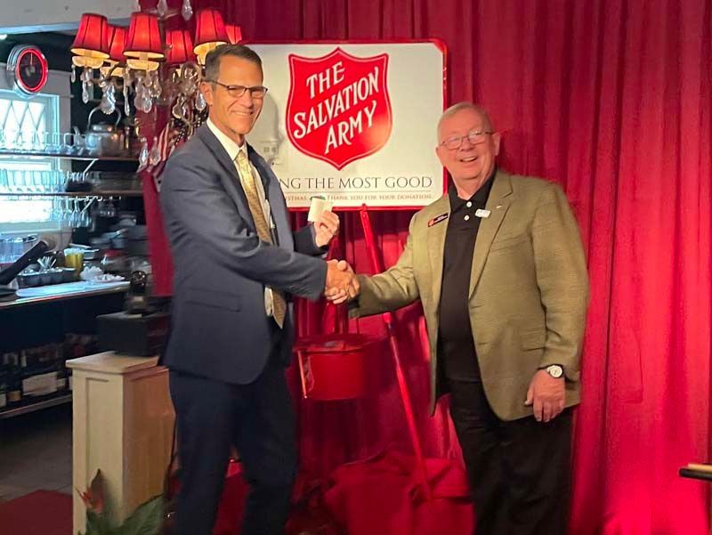 Two men shaking hands in front of a red Salvation Army backdrop