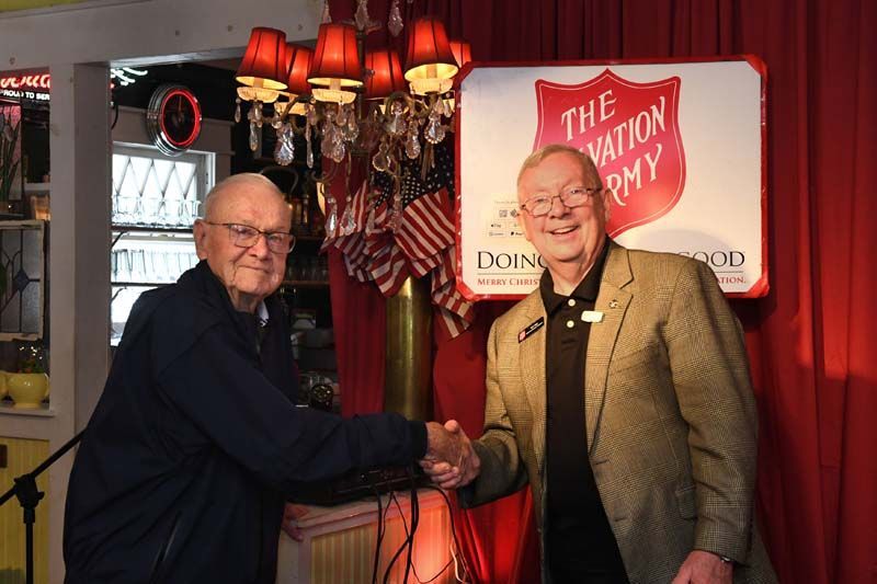 Two men shaking hands in a warmly lit restaurant beside a Salvation Army sign.
