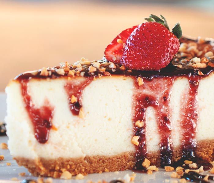 Creamy cheesecake slice topped with strawberry sauce, nuts, and a fresh strawberry