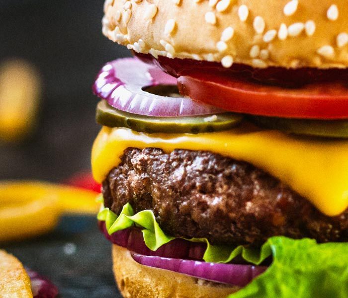 Close-up of a cheeseburger with sesame bun, melted yellow cheese, tomato, onion, and lettuce