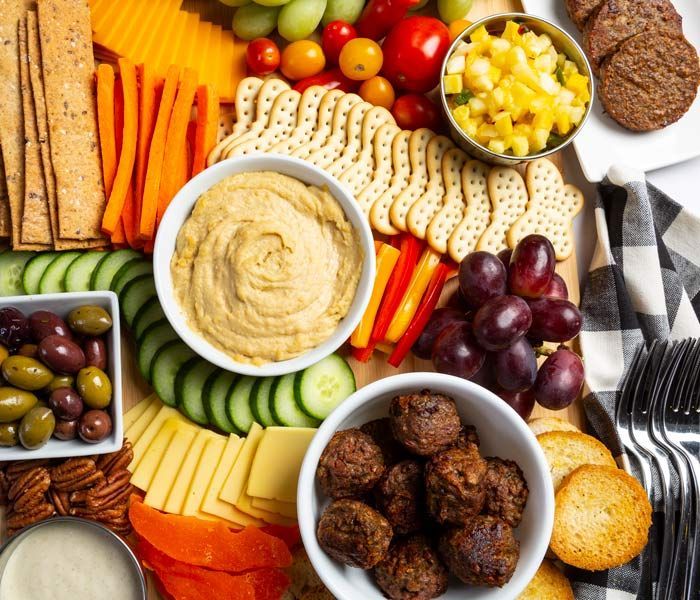 Charcuterie board with hummus, crackers, vegetables, fruit, cheese, olives, and meatballs