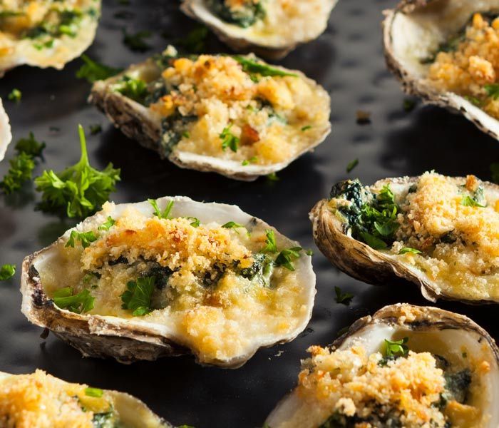 Baked oysters topped with breadcrumbs and herbs on a dark serving tray
