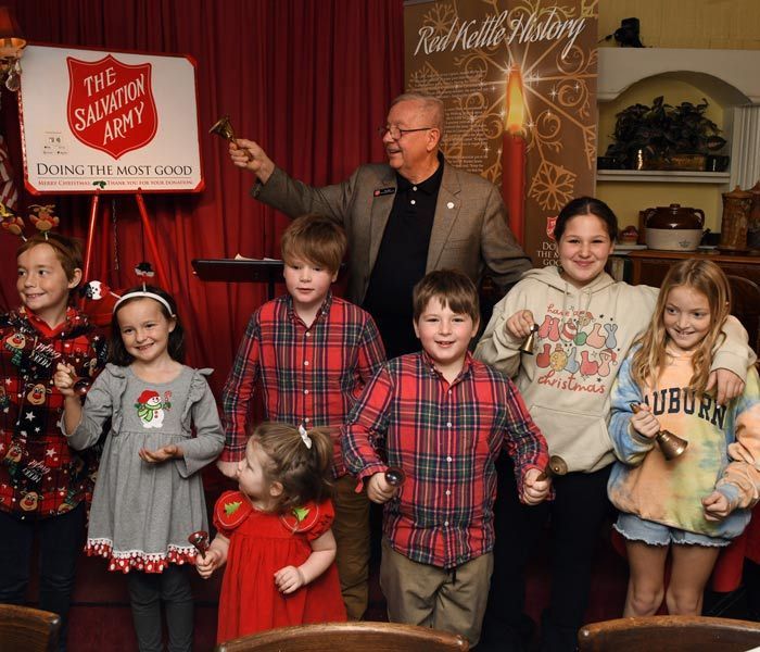 Children posing on stage with a host in front of red curtains and holiday decorations