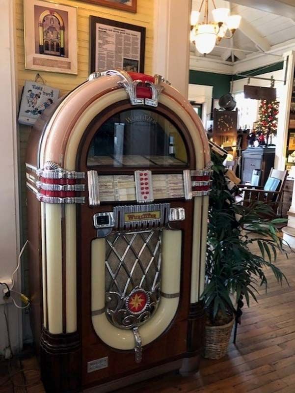 Vintage jukebox in a warmly lit room with framed art and a potted plant nearby