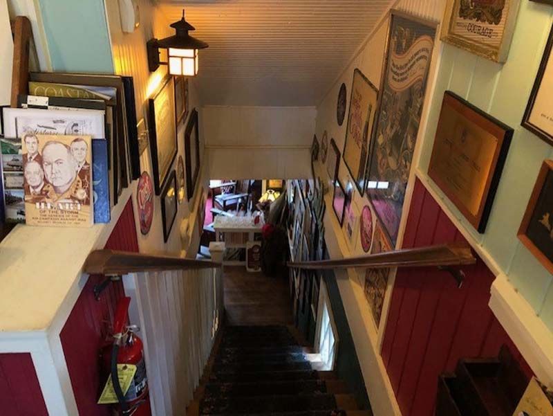 Narrow indoor stairway lined with framed art and warm wall lights, descending to a lower level.