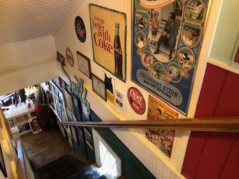 Staircase wall lined with colorful vintage Coca-Cola signs and ads in a narrow interior hallway