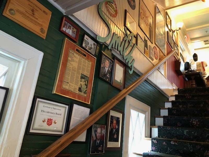 Stairway wall lined with framed awards and certificates, with people ascending the stairs.