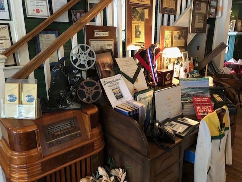 Cluttered vintage display of radios, film reels, books, and lamps in a shop or museum corner