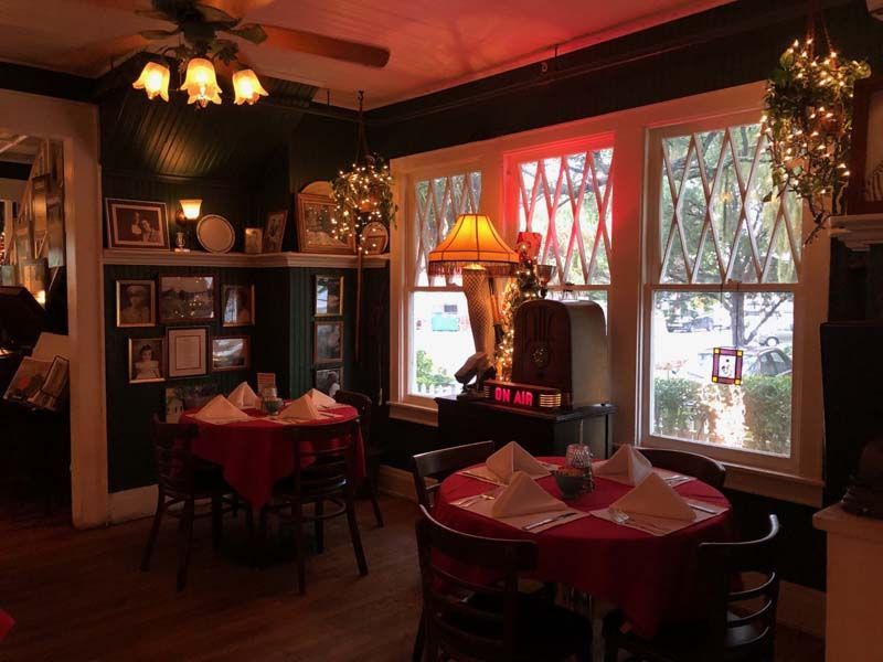 Cozy dimly lit restaurant interior with red tablecloths, warm lamps, and windows overlooking trees
